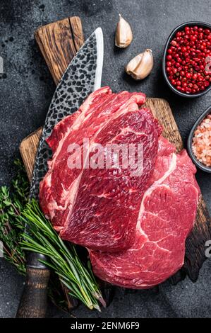 Rouleau de Chuck Eye cru steak de bœuf Black Angus de qualité sur le plateau de boucher avec couteau. Arrière-plan noir. Vue de dessus Banque D'Images