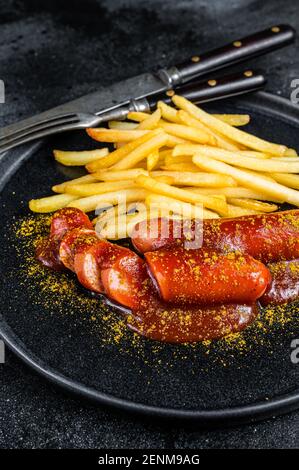 Saucisses de currywurst allemandes avec frites sur une assiette. Arrière-plan noir. Vue de dessus Banque D'Images