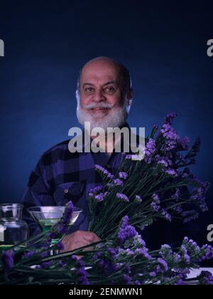 Portrait d'un homme âgé dans des tons bleus tenant un bouquet de fleurs bleues et violettes Banque D'Images