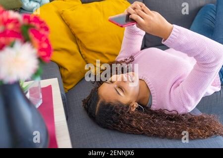 Un jeune latin souriant s'étendait sur le canapé d'elle maison comme elle parle sur le téléphone cellulaire Banque D'Images