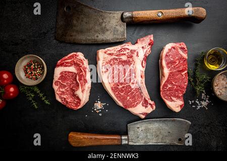 Variété de steaks de viande de bœuf Angus noir frais et cru, os de T, New York, Ribeye et assaisonnement sur fond noir, vue du dessus
