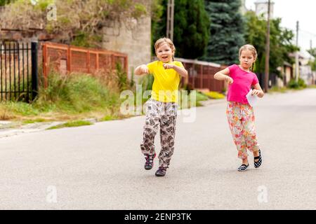 Des jeunes enfants heureux dans la rue de la ville, deux jeunes filles gaies et gaies en âge d'aller à l'école sautant, marchant dans la rue ensemble frères et sœurs, sœurs ou amies Banque D'Images