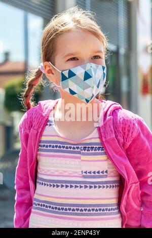 Bonne joyeuse petite fille, enfant d'âge scolaire portant un masque protecteur souriant, portrait, vertical. Enfant dans un masque coloré, virus corona, covid Banque D'Images