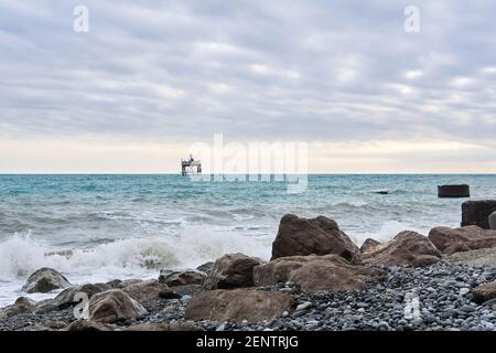 plage d'hiver avec paysage marin et une structure rickety sur le pilotis d'une ferme de mariculture au loin Banque D'Images