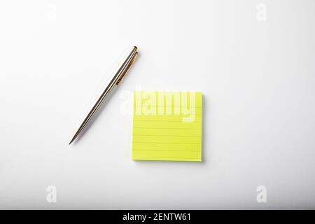 Bloc-notes adhésif carré jaune fluorescent avec stylo à bille argenté sur fond blanc. Banque D'Images