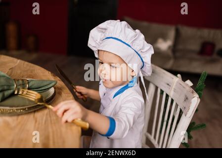 Concept de saine alimentation. Un petit garçon heureux cuisine dans la cuisine par une belle journée d'été. Lors d'un pique-nique, le boulanger mange du pain et des bagels dans un tablier blanc Banque D'Images