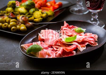 Prosciutto avec différents hors-d'œuvre avec un verre de vin rouge sur fond noir. Sur les légumes rôtis, en-cas sain Banque D'Images