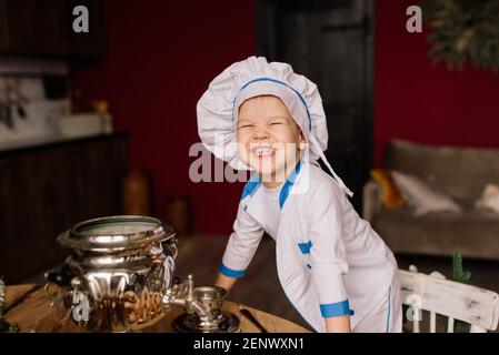 Concept de saine alimentation. Un petit garçon heureux cuisine dans la cuisine par une belle journée d'été. Lors d'un pique-nique, le boulanger mange du pain et des bagels dans un tablier blanc Banque D'Images