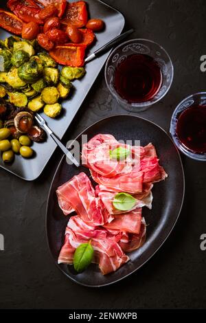 Prosciutto avec différents hors-d'œuvre avec un verre de vin rouge sur fond noir. Sur les légumes rôtis, en-cas sain Banque D'Images