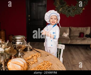 Concept de saine alimentation. Un petit garçon heureux cuisine dans la cuisine par une belle journée d'été. Lors d'un pique-nique, le boulanger mange du pain et des bagels dans un tablier blanc Banque D'Images