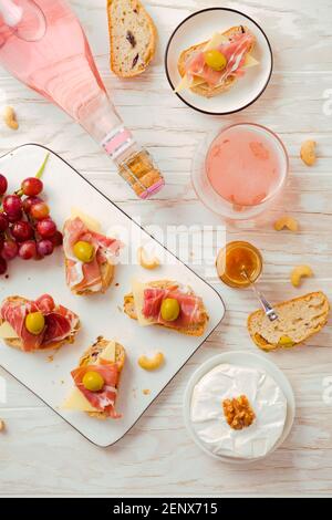 Plats de hors-d'œuvre et sandwichs ouverts avec antipasti italiens, camembert, jambon de Parme et vin de rose sur une table en bois Banque D'Images