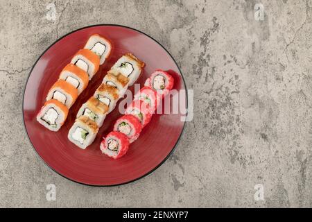 Assiette rouge de divers délicieux petits pains à sushis sur fond de marbre Banque D'Images