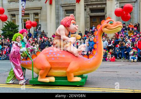 Caveman à cheval sur un mini-flotteur de dinosaure dans la célébration de la 109e édition de la Parade du Père Noël. Plus d'un demi-million de personnes suivent le même cours Banque D'Images