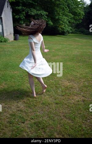 Une jeune fille dans une robe blanche tourne en cercles dans un cadre rustique de cour arrière. Banque D'Images