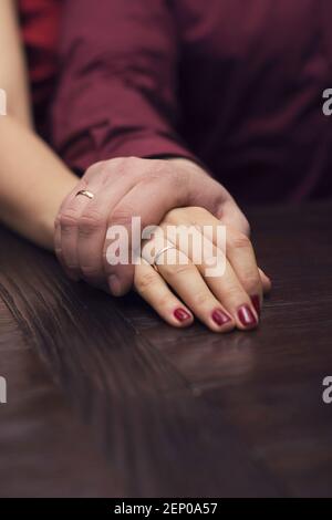Couple marié tenant les mains avec des anneaux sur la table. Couleurs veineuses Banque D'Images