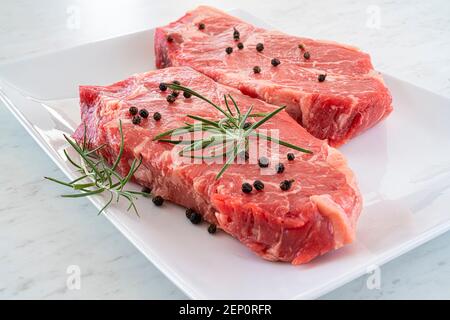 Steak de stripilline de bœuf marbré garni de romarin et de grains de poivre sur une assiette blanche. Banque D'Images