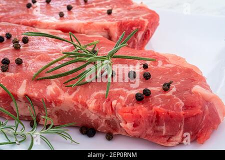 Steak de stripilline de bœuf marbré garni de romarin et de grains de poivre sur une assiette blanche. Banque D'Images