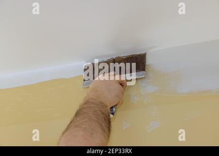 Un constructeur professionnel lisse le mur avec du mastic à la spatule placé sur une surface plane de réparation de mur dans son propre appartement. Banque D'Images