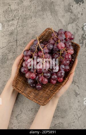 Femme tenant main panier de raisins rouges sur fond de marbre Banque D'Images