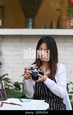 Portrait d'une jeune femme artiste ou photographe qui vérifie la photo sur l'appareil photo lorsqu'elle est assise à son atelier. Banque D'Images