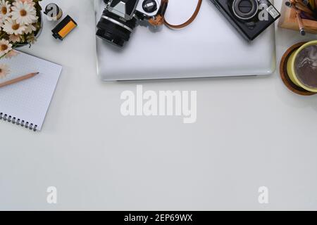 Vue aérienne de l'espace de travail du photographe avec ordinateur portable, appareil photo, ordinateur portable, tasse à café et espace de copie sur table blanche. Banque D'Images