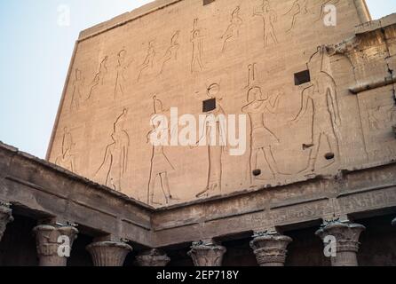 Temple Edfu - façade nord de l'aile est du Grand Pylon avec les reliefs du roi Ptolémée XII en interaction avec les dieux Horus et Hathoror. Banque D'Images