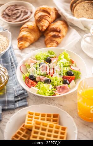 Petit déjeuner copieux avec salade, croissants, gaufres, pain et jus d'orange Banque D'Images
