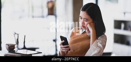 Image horizontale d'une jeune femme agacée et frustrée qui regarde le smartphone se sentir insatisfait de l'e-mail reçu. Banque D'Images