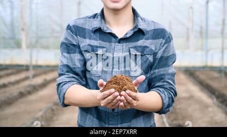 Jeune agronome masculin tenant le sol et examinant la qualité du champ agricole fertile. Banque D'Images