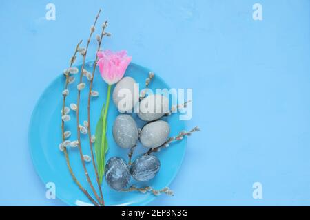 Vacances de Pâques.oeufs gris en marbre de Pâques, brindilles de saule et fleur de tulipe rose dans une assiette bleue sur fond bleu clair. Nourriture de Pâques. Religieux de printemps Banque D'Images