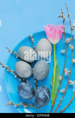 Easter.Easter les oeufs gris en marbre, les brindilles de saule et la fleur de tulipe rose dans une assiette bleue sur un fond bleu clair. Nourriture de Pâques. Vacances religieuses de printemps Banque D'Images