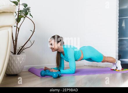 la jeune fille est engagée dans le sport à la maison. une jeune femme dans un survêtement bleu fait une planche sur un tapis de gym. fitness à la maison Banque D'Images