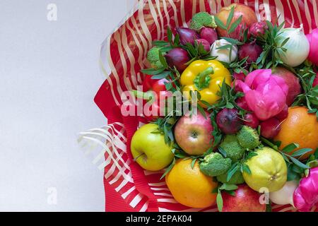 Un magnifique bouquet coloré de fruits frais, légumes et fleurs entouré de rouge et transparent avec du papier blanc rayé sur un dos beige Banque D'Images