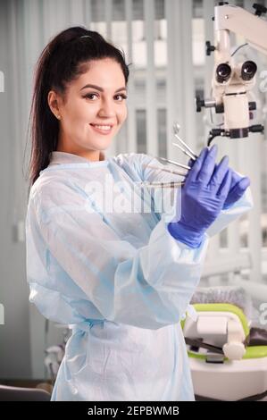 Portrait de jolie femme dentiste porte des outils pour le traitement dentaire dans des gants bleus stériles. Femme dentiste regardant la caméra et souriant tout en faisant la démonstration des instruments dentaires. Concept de la dentisterie. Banque D'Images