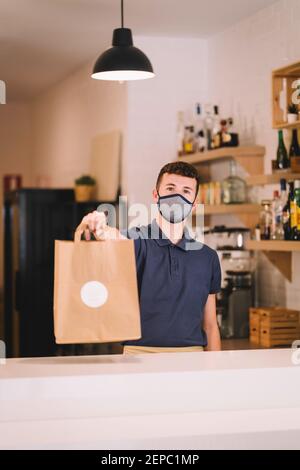 portrait d'un serveur professionnel avec masque qui livre un sac en papier recyclé avec une commande à emporter dans un restaurant pendant une pandémie de coronavirus. Banque D'Images