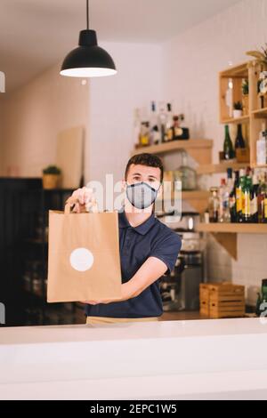 portrait d'un serveur professionnel avec masque qui livre un sac en papier recyclé avec une commande à emporter dans un restaurant pendant une pandémie de coronavirus. Banque D'Images