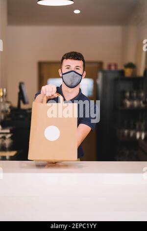 portrait d'un serveur professionnel avec masque de remise d'un sac en papier recyclé avec commande à emporter pendant une pandémie de coronavirus Banque D'Images