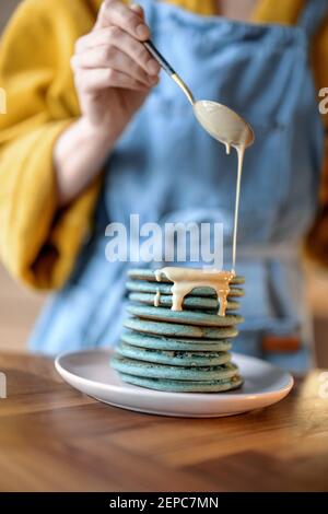 Femme versant des crêpes bleues avec une souse au caramel. Banque D'Images