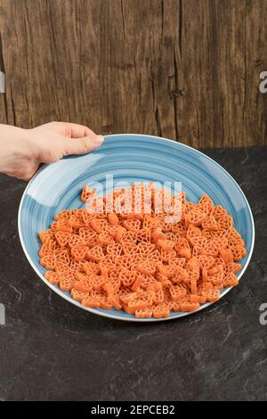 Femme main tenant une assiette avec des pâtes crues dans le coeur forme sur table noire Banque D'Images