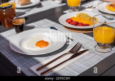 Le petit-déjeuner est servi sur une table, avec un œuf sur une assiette, des fruits, du jus d'orange et du café. Gros plan. Banque D'Images