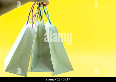 Photo courte de la main femelle tenant un bouquet de différents sacs de shopping vierges colorés sur fond jaune isolé. Concept de solde du Vendredi fou. Copie s Banque D'Images