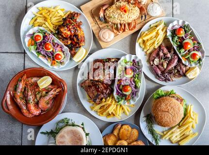 Diverses assiettes de cuisine méditerranéenne et occidentale allant de crevettes, crabe, calmar, côtes, un hamburger, beaucoup de salade et de frites. Banque D'Images