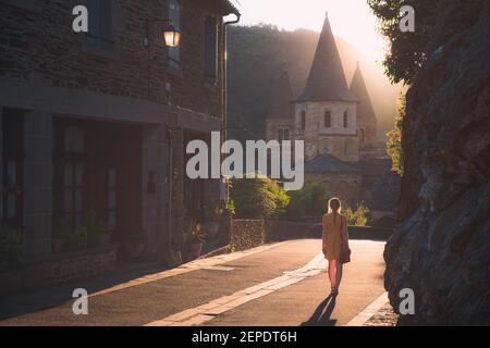 Une jeune touriste féminine en robe d'été explore le pittoresque et charmant village médiéval français de Conques, Aveyron au coucher du soleil ou au lever du soleil à Occitani Banque D'Images