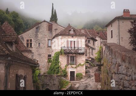 Le pittoresque et charmant village médiéval français au sommet d'une colline de Saint-Cirq-Lapopie lors d'une matinée brumeuse dans la vallée du Lot, en France. Banque D'Images