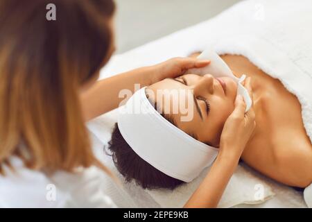 Une esthéticienne féminine lave le visage d'un client de femme se préparant à une procédure cosmétique. Banque D'Images