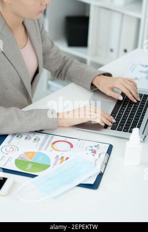 Mains de jeune femme d'affaires contemporaine ou secrétaire dans l'élégant gris convient aux touches du clavier de l'ordinateur portable lors de la mise en réseau au bureau Banque D'Images