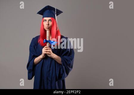 Une jeune femme triste, diplômée d’université, pense à son futur emploi. portrait de studio sur fond gris. Banque D'Images