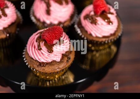 Des cupcakes au chocolat gourmets, arrosés de ganache au chocolat et recouverts d'une framboise fraîche. Banque D'Images