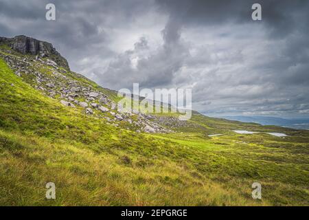 Vert, herbe longue, gros rochers et décombres sur le flanc de montagne de Cuilcagh avec de petits lacs dans la vallée en dessous, Irlande du Nord Banque D'Images