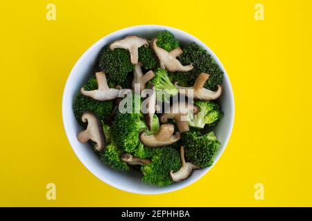Salade végétarienne avec shiitake aux champignons et brocoli dans le bol blanc sur fond jaune.vue du dessus.espace de copie.ingrédients alimentaires sains. Banque D'Images